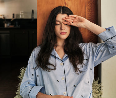 an image of a woman wearing blue pajamas with her eyes closed and one hand against her forehead.