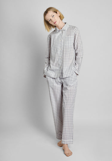 A woman wearing a long sleeve and pants grey and white gingham pajama set in front of a plain background.