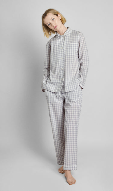 A woman wearing a long sleeve and pants grey and white gingham pajama set in front of a plain background.