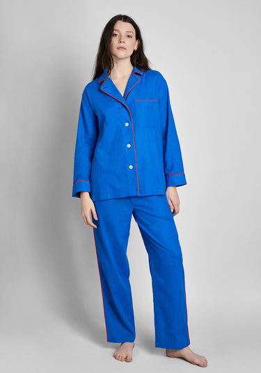 A woman wearing a two-piece blue linen pajama set with red/orange piping and white buttons.