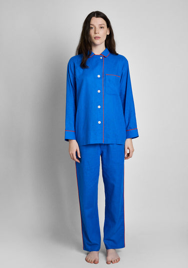 a woman wearing blue linen button-up pajamas with orange/redish piping. 
