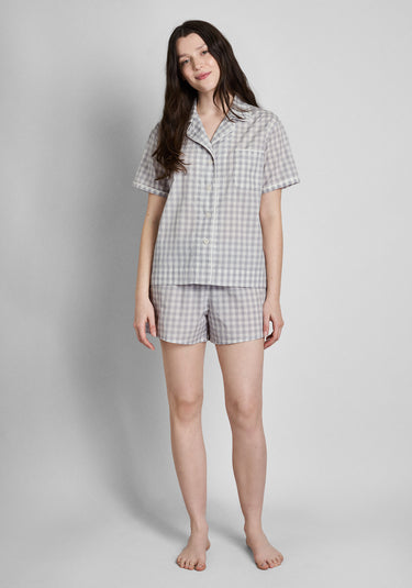 A woman wearing a short sleeve and shorts grey and white gingham pajama set in front of a plain background.