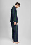 Man wearing a green and navy blackwatch plaid pajama set on a light grey background