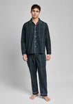 Man wearing a dark green and navy blackwatch plaid pajama set on a gray background