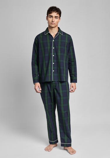 Man wearing a dark green and navy blackwatch plaid pajama set on a gray background