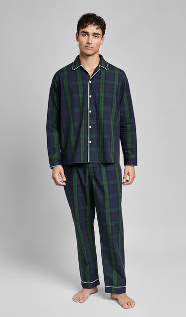 Man wearing a dark green and navy blackwatch plaid pajama set on a gray background