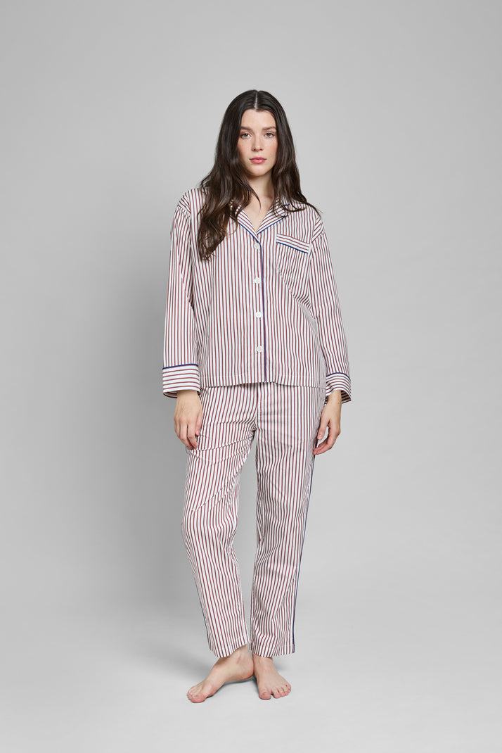 Woman wearing a burgundy and white striped pajama set with blue piping on a gray background