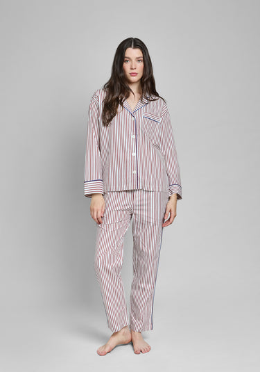 Woman wearing a burgundy and white striped pajama set with blue piping on a gray background