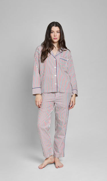 Woman wearing a burgundy and white striped pajama set with blue piping on a gray background