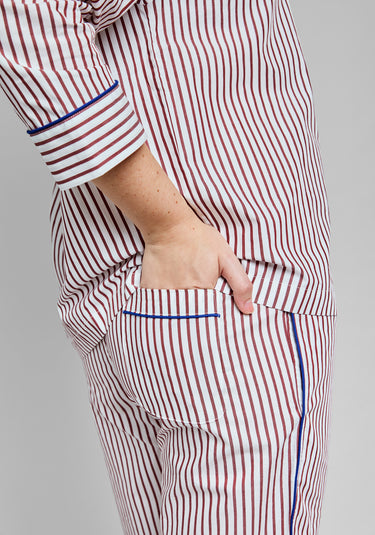 Burgundy and white striped pajama set with blue piping on a gray background