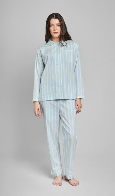 Woman wearing a light blue, tan, and cream striped pajama set on a gray background