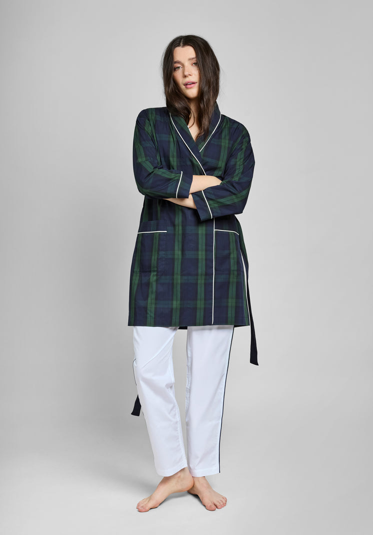 Woman wearing a green and navy blackwatch plaid robe with white piping over white pants on a gray background