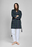 Woman wearing a green and navy blackwatch plaid robe with white piping over white pants on a gray background