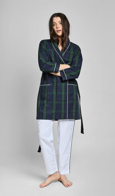 Woman wearing a green and navy blackwatch plaid robe with white piping over white pants on a gray background