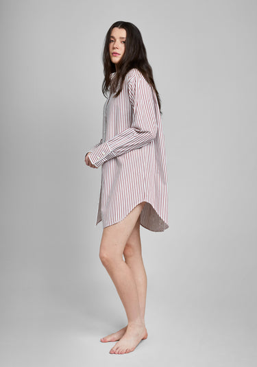 Woman wearing a burgundy and white striped long sleeve shirt dress on a gray background
