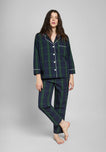 Woman wearing a green and navy blackwatch plaid pajama set with white piping details on a grey background