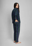 Woman wearing a green and navy blackwatch palid pajama set on a gray background. Her hand is in her back pocket.