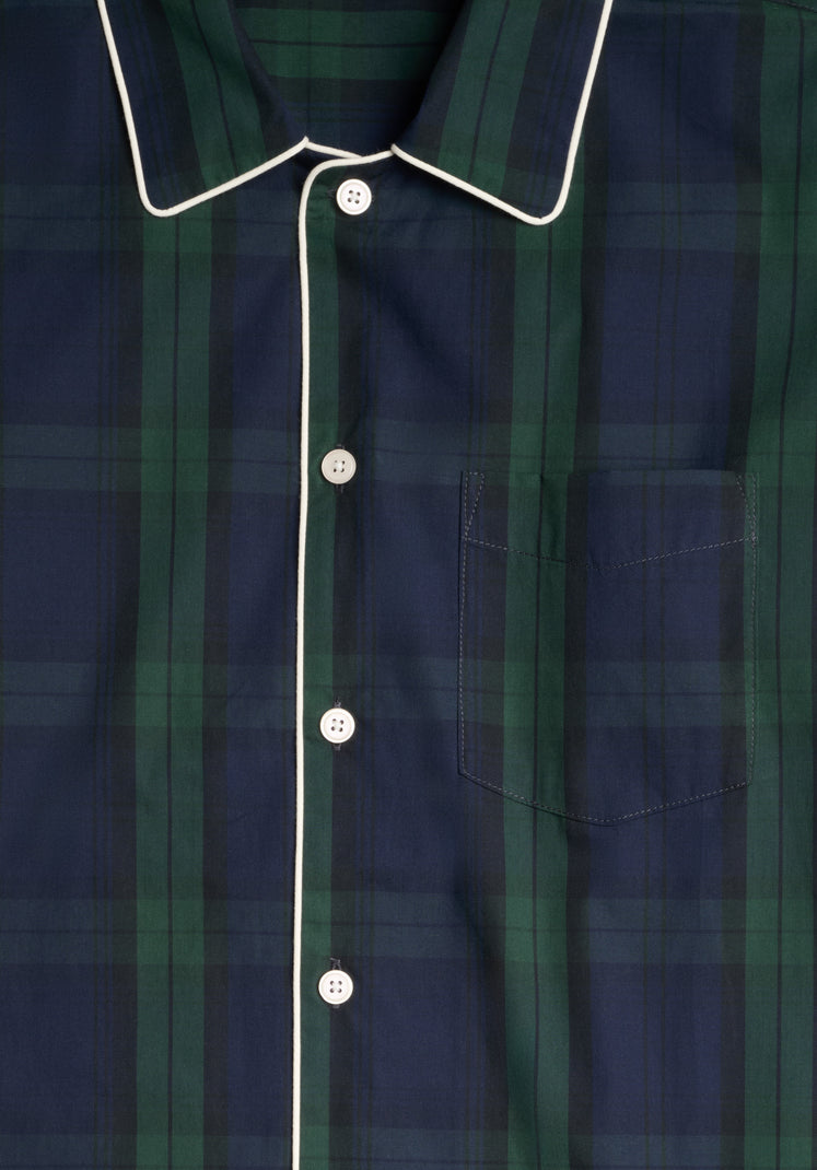 Close up collar detail of a navy and green blackwatch plaid shirt with white buttons and trim and a chest pocket.
