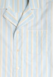 Close up of the collar and pocket detail of a light blue pajama set with cream and tan stripes and white piping.