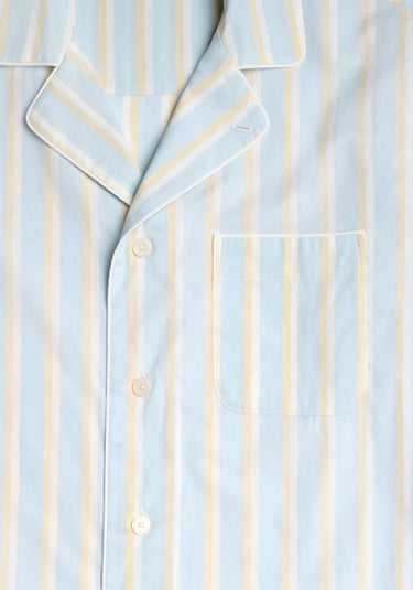 Close up of the collar and pocket detail of a light blue pajama set with cream and tan stripes and white piping.
