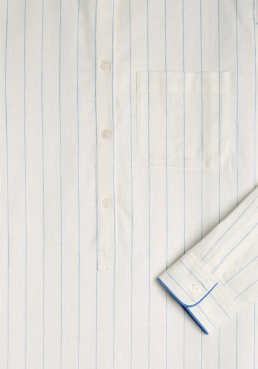 A detail image of the Georgia Kaftan in linen. A light cream lien fabric with a thin blue stripe. Detail image shows pocket, and button placket, and arm cuff with light blue piping.