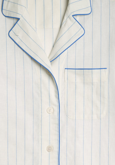 A detail image of the pajama set, a light cream pajama set with blue stripes, blue piping, and a chest pocket.