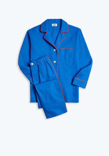 A blue long-sleeve linen Margaret pajama set with orange-red piping details on a white background, consisting of a top and pants.
