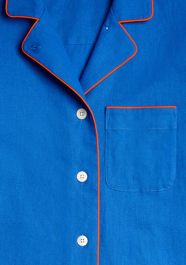 a close up detail image of the collar of the blue linen pajama set featuring white buttons and red/orange piping