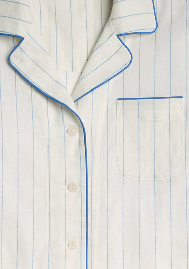 A detail image of the pajama set, a light cream pajama set with blue stripes, blue piping, and a chest pocket.