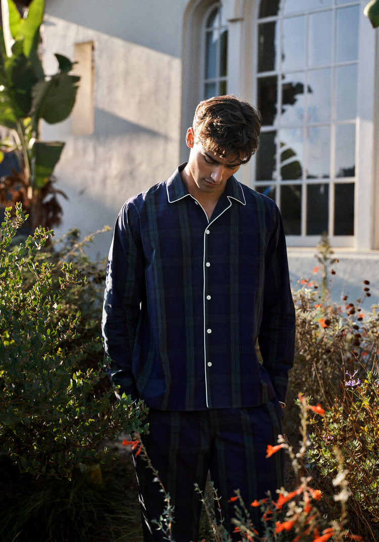 man wearing a navy and green blackwatch pajama set with white trim in a garden setting