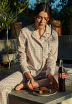 Woman sitting outdoors in grey gingham pajamas with a plate of cookies and a bottle of soda.