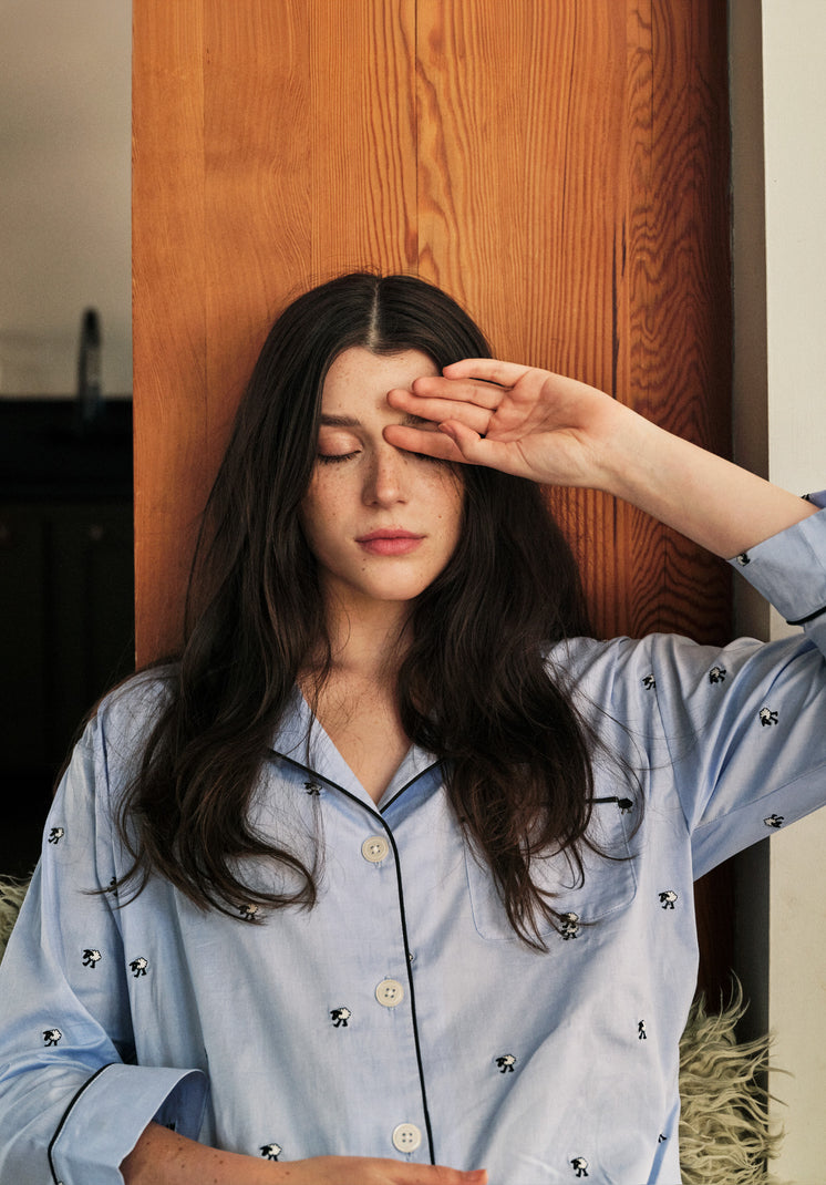 A woman wearing blue pajamas with sheep on them closing her eyes with one hand resting against her forehead.