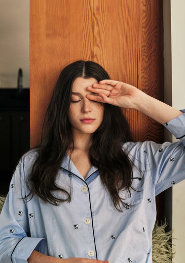 A woman wearing blue pajamas with sheep on them closing her eyes with one hand resting against her forehead.