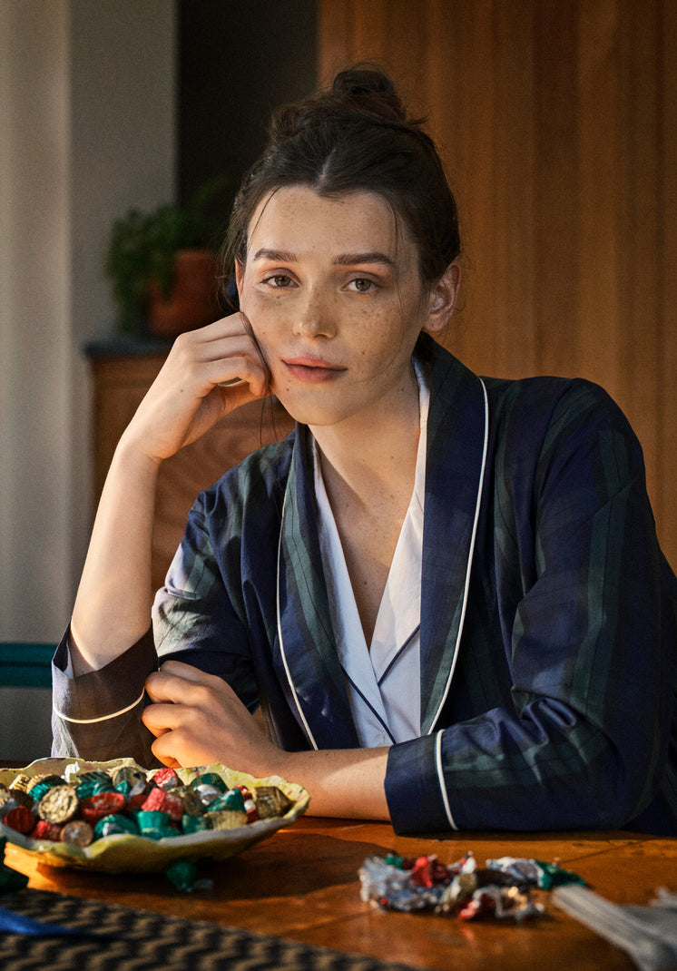 Woman in a blackwatch robe sitting at a table with a bowl full of wrapped chocolates.