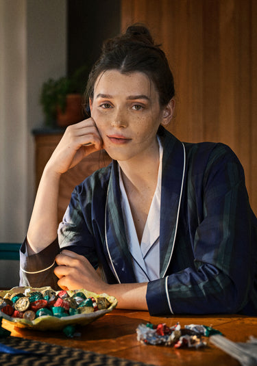 Woman in a blackwatch robe sitting at a table with a bowl full of wrapped chocolates.