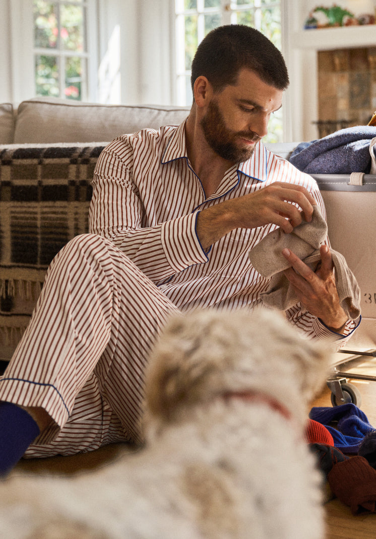 Man in striped pajama set sitting on a couch with a dog, holding  pair of socks.
