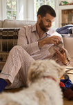 Man in striped pajama set sitting on a couch with a dog, holding  pair of socks.