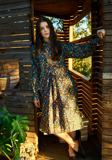 Woman sitting in the doorway of an outdoor structure wearing a long floral dress.